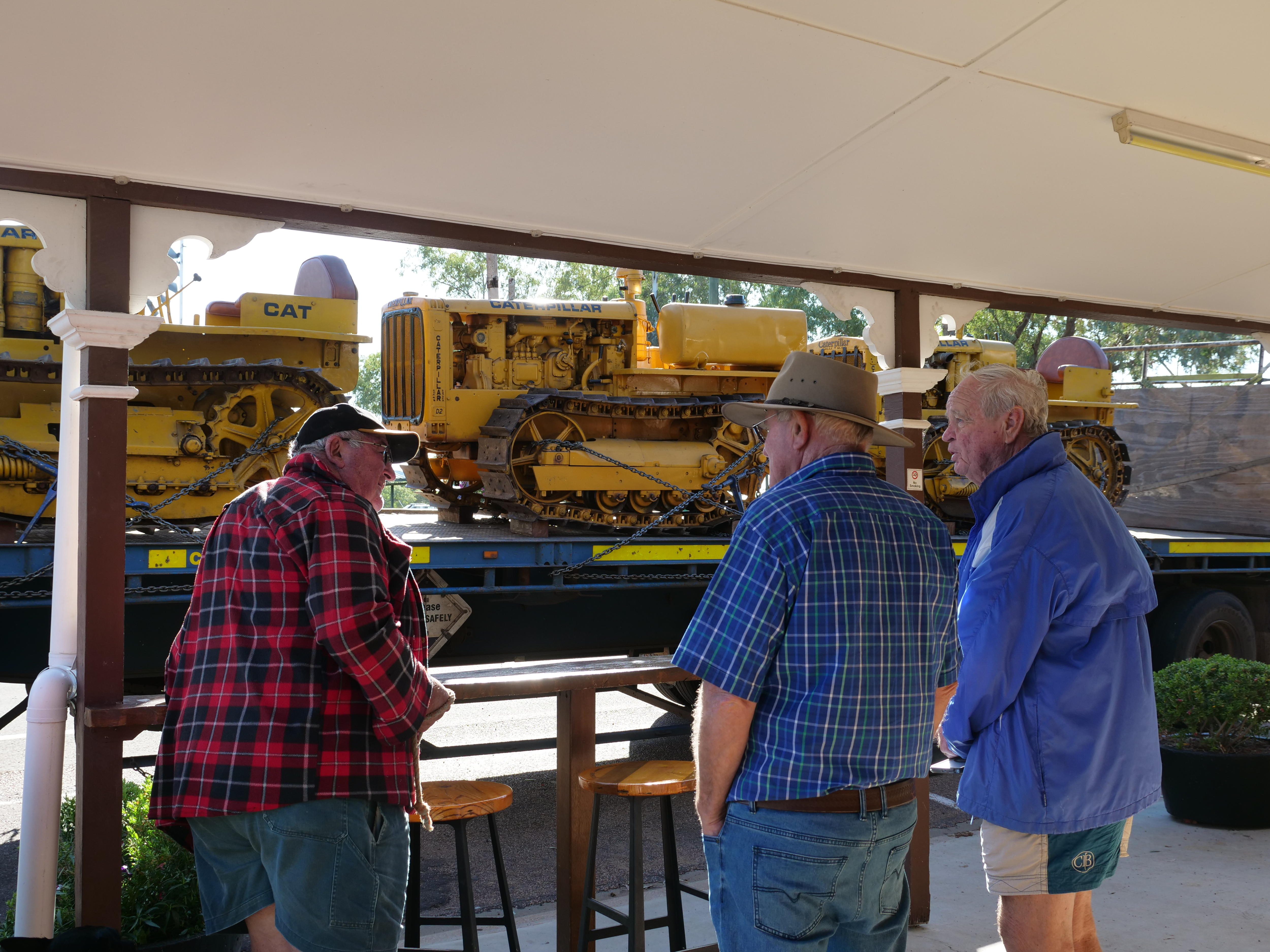 three people under a canopy chatting and looking at yellow tractor