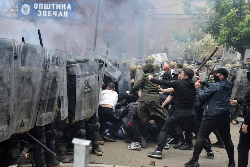 A group of civilians attack soldiers in riot gear. 