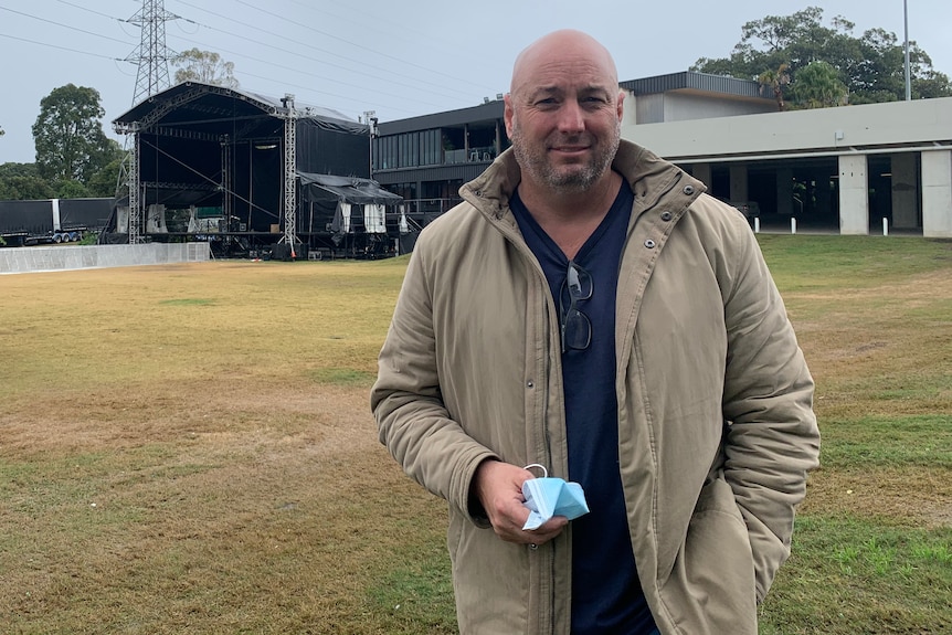 Bald man stands on grass outside a building