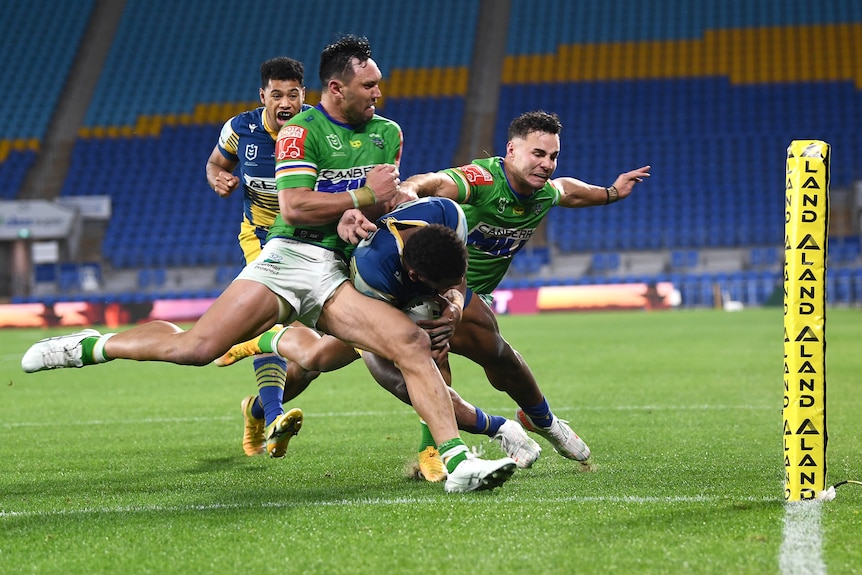 Two defenders tackle a rugby league ball runner over the sideline has he attempts to score a try in the corner.