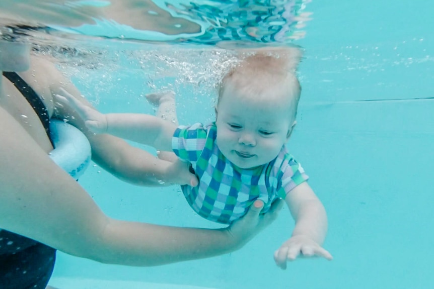 A baby held by a woman swims in a pool.