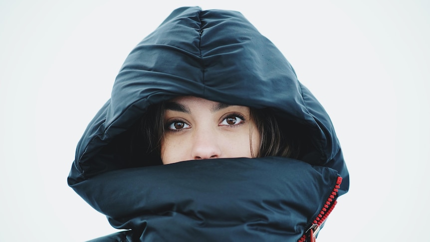 Face of woman in hoodie with a puffer jacket against a white background 