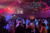 People dance under coloured lights in a big airport hanger space.