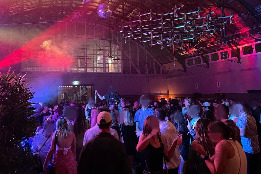 People dance under coloured lights in a big airport hanger space.