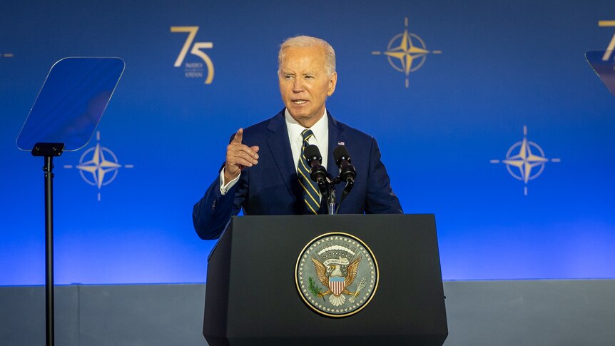 Joe Biden speaks at a podium and gestures with his right hand as he reads off a teleprompter