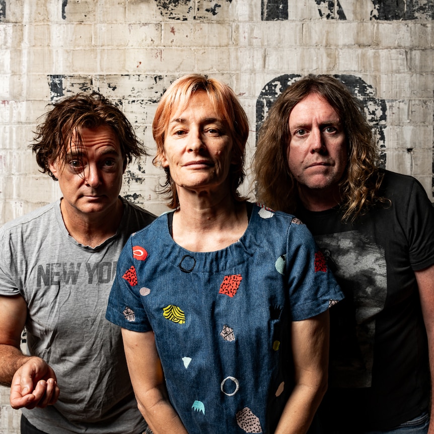 The three members of Spiderbait pose in front of a white-washed brick wall