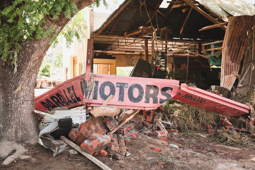 Red and black sign with the text 'parallel motors' lays twisted and bent on top of a pile of damaged bricks