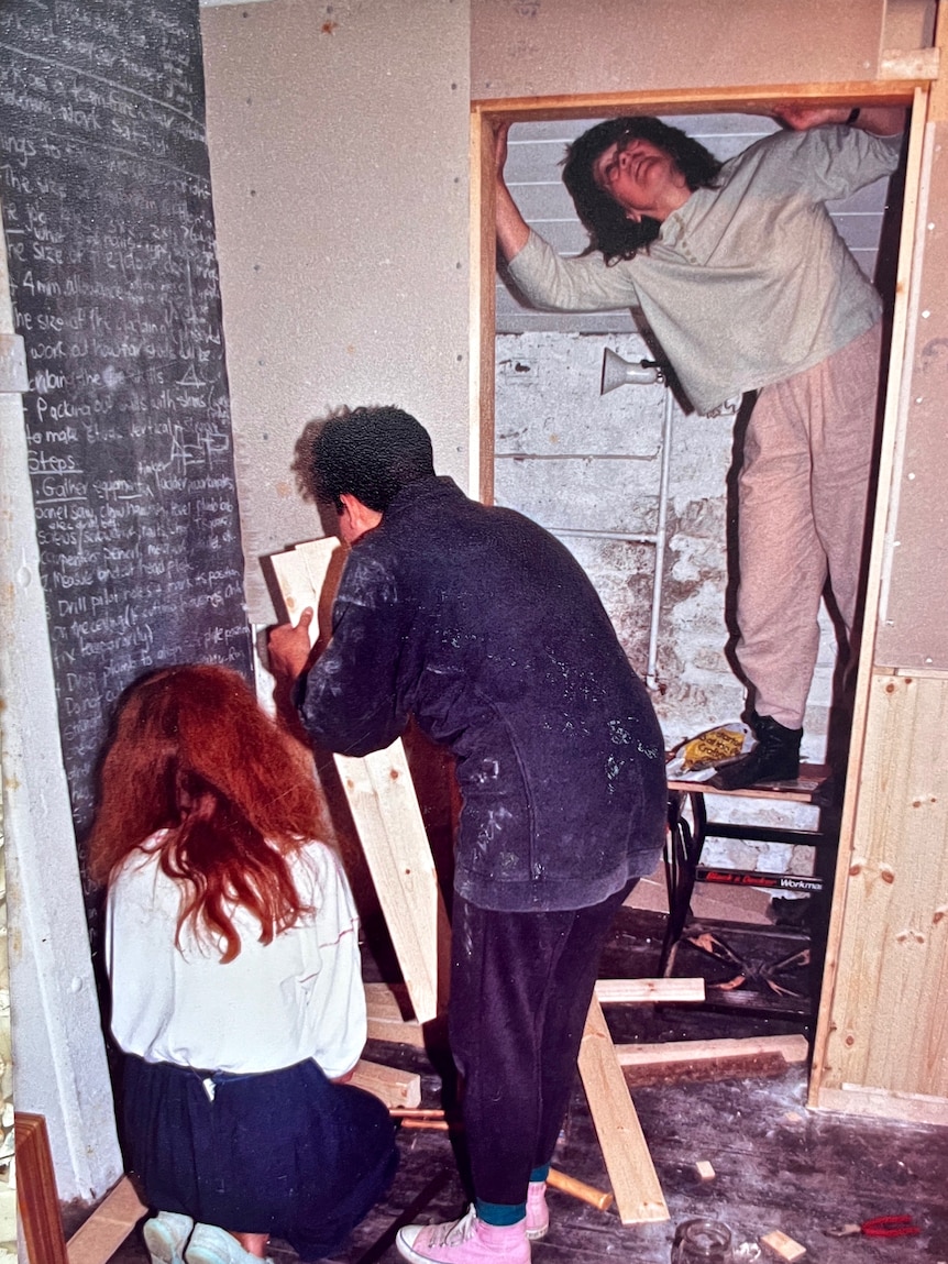 An old photograph of three women huddled in a small room making adjustments to wooden features.