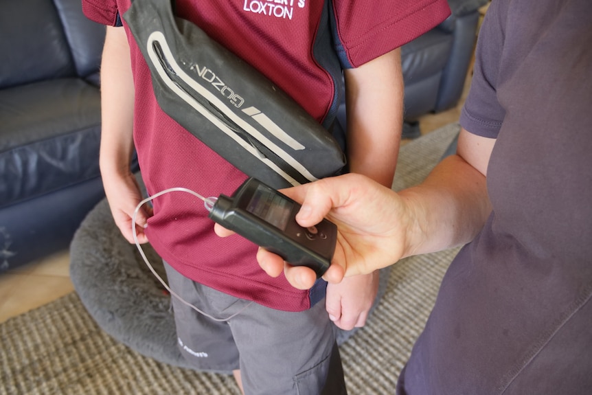A womans hand holds a black monitor with a clear tube which connects to a childs body in a school uniform
