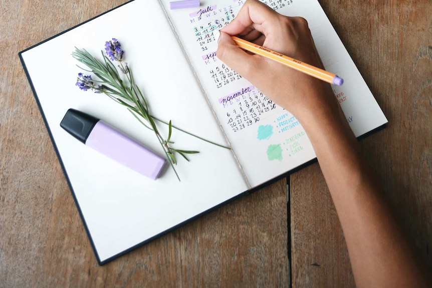 Woman marking down dates in her calendar notebook, with a purple highlighter and lavender as props on her notebook.