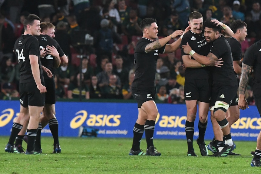 All Black players embrace and smile in celebration after beating South Africa in a rugby union international.