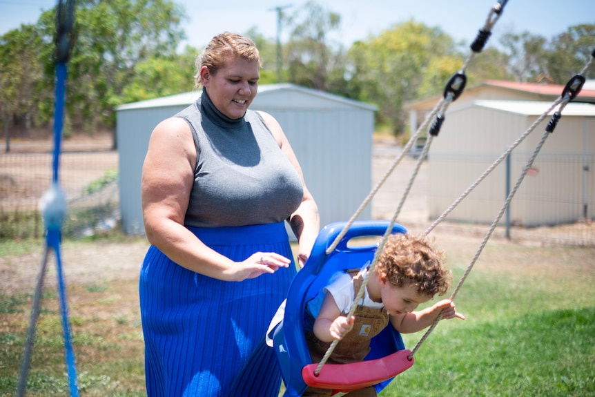 A woman pushing her toddler son on a swing set in a residential backyard.