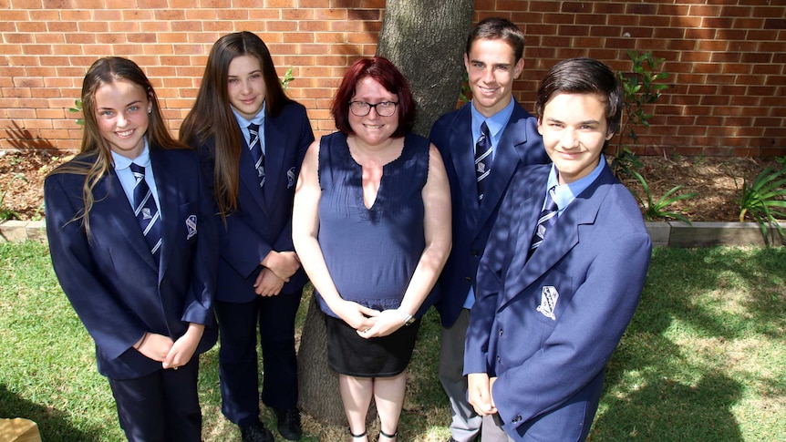Four debating students from Keira High School stand with their teacher under a tree.