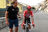 Caleb Ewan looks disappointed on his bike, next to a man in a black shirt