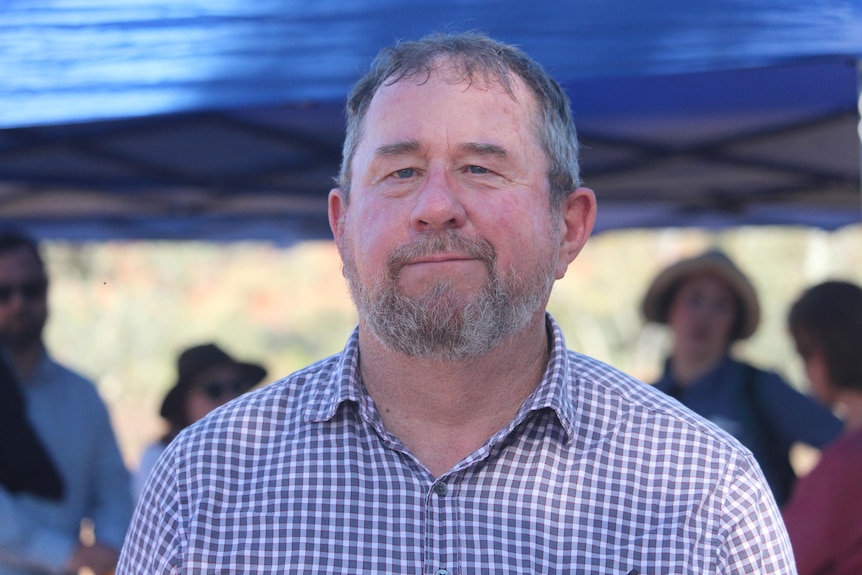 A man in a checkered shirt stares happily at the camera