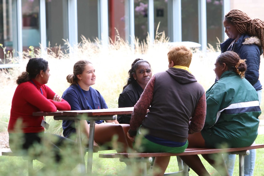 The six young members of the Connecting to Culture group involved in a discussion, gathered around an outdoor table in Canberra.