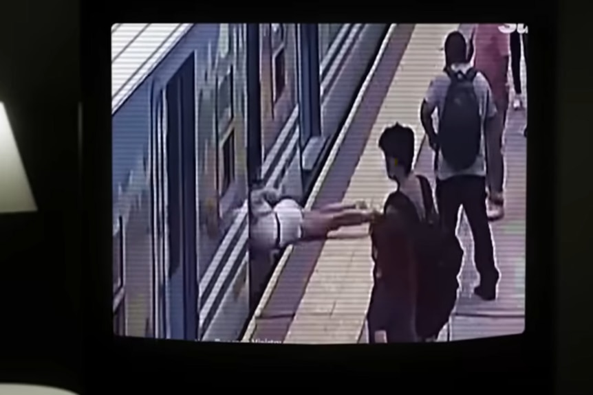 Grainy footage on a tv shows a man falling towards a train