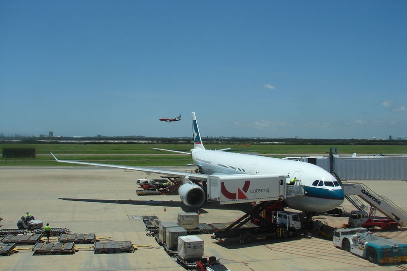 Jet parked next to airbridge at Brisbane international airport, with Virgin plane landing in backgrd