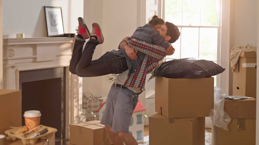 A young couple embrace happily inside their new home, surrounded by moving boxes.