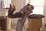 A young couple embrace happily inside their new home, surrounded by moving boxes.