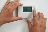 A person uses their fingers to turn up a heater on a wall.