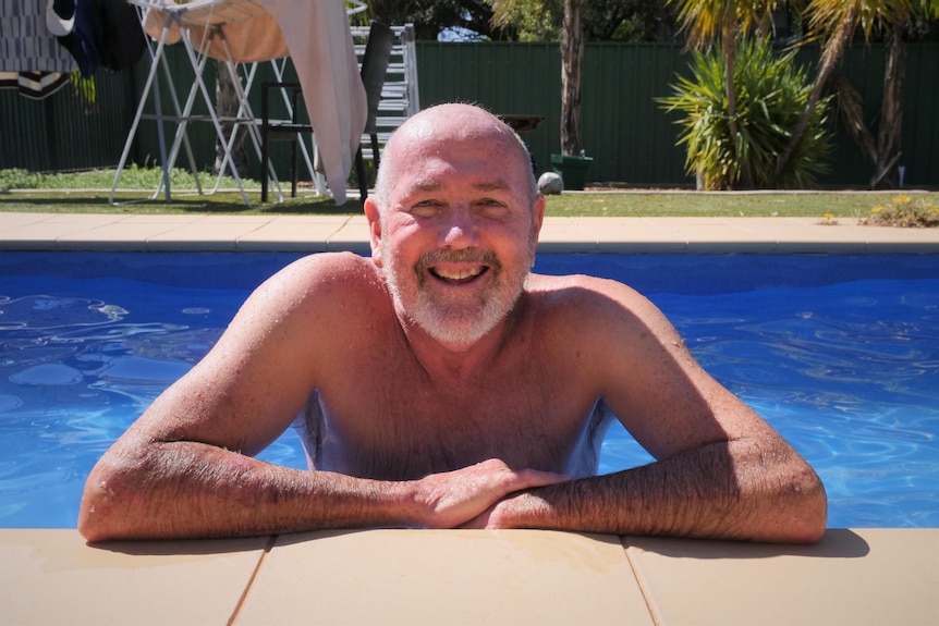 Man leaning over swimming pool edge, smiling at camera
