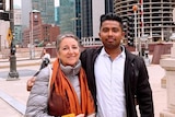 Faisal Parvez stands next to his teacher in front of skyscrapers.