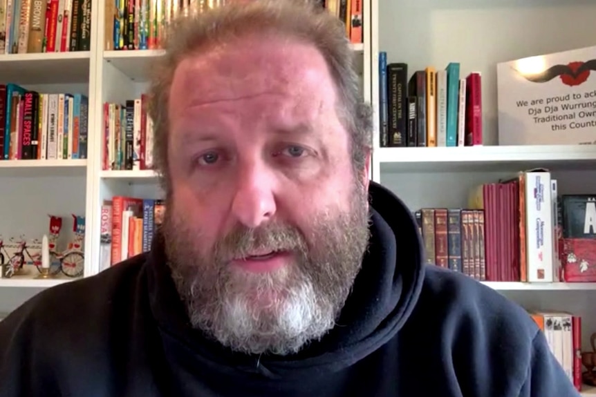 Josh Cullinan sits in front of a bookshelf.