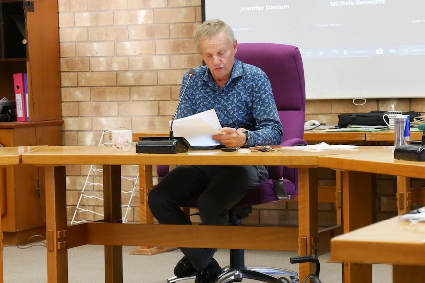 A man sits at a long desk looking through council papers.