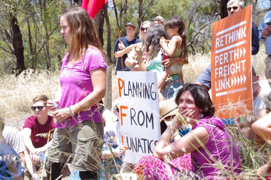 A group of protesters with placards and flags sit in bushland at Bibra Lake.