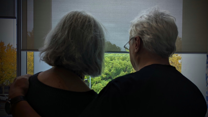 Dark silhouetted photo of a man and a woman looking out a window, taken from behind.