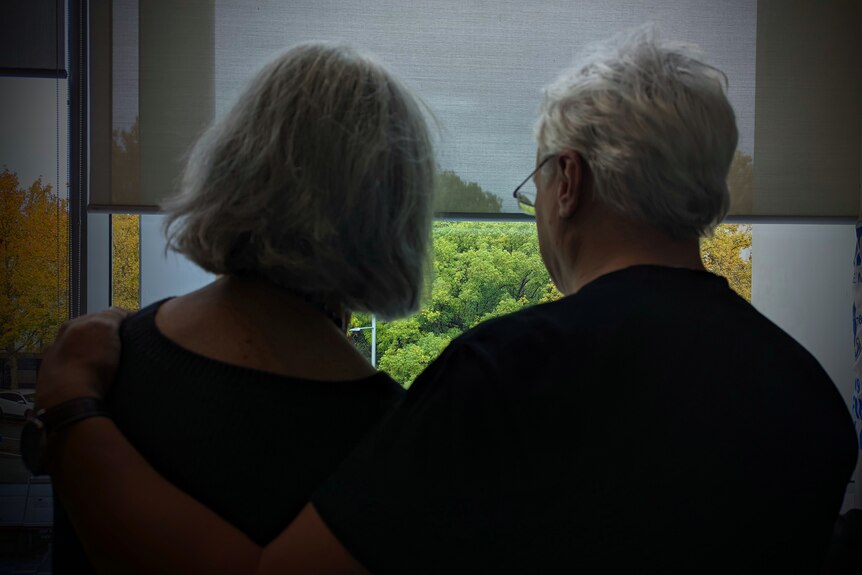 Dark silhouetted photo of a man and a woman looking out a window, taken from behind.
