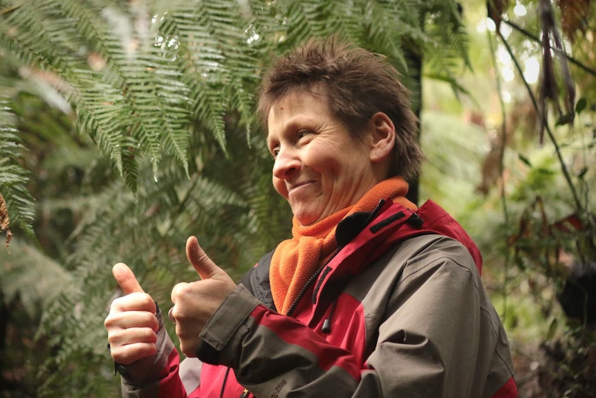 Di Crowther giving the thumbs up standing in front of ferns