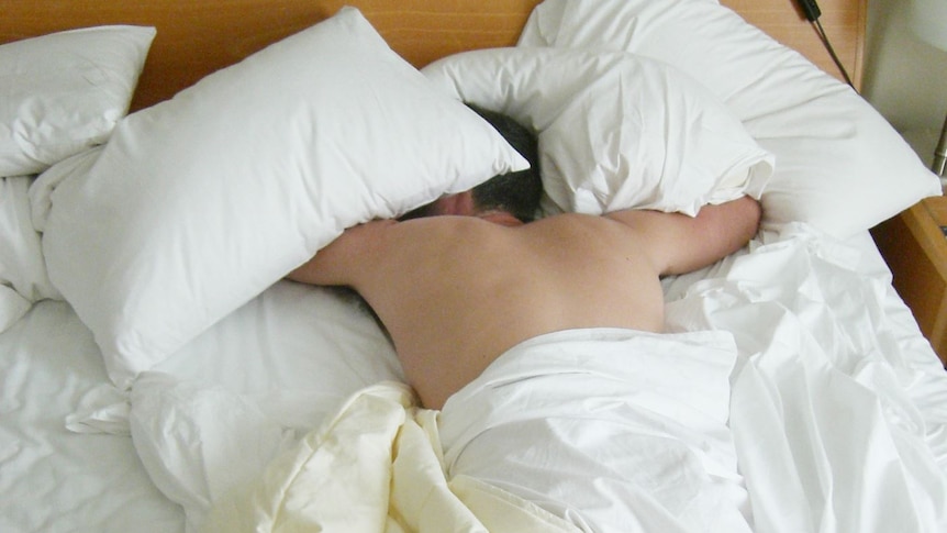 A man sleeping in a messy bet with white bedding.