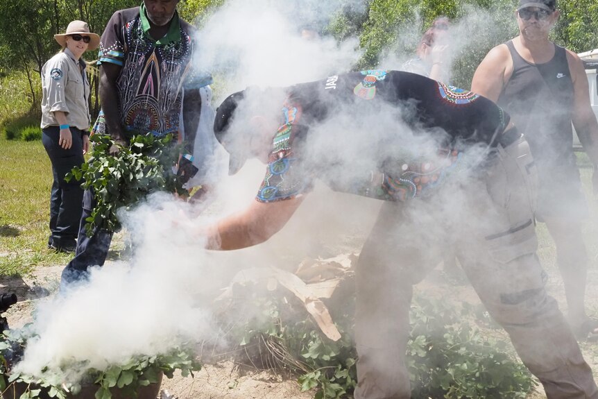 A man stands in smoke, fanning leaves in a smoking ceremony.