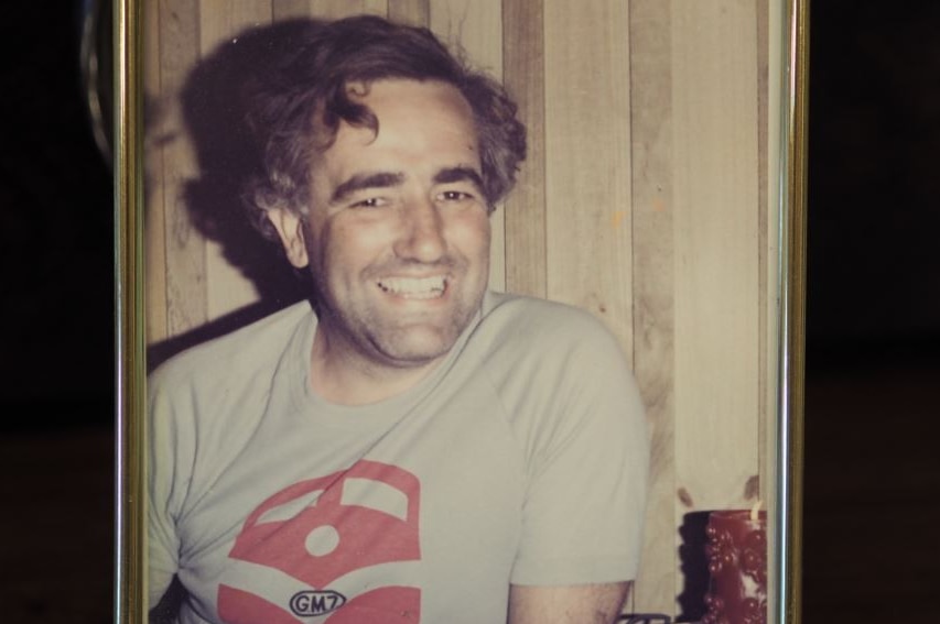 Kenneth Stirling sitting in front of a wooden wall smiling