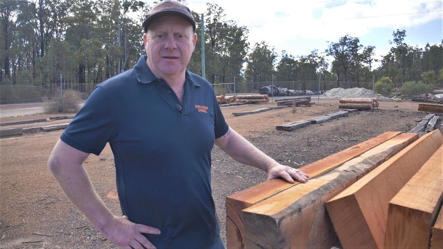 man stands in yard leaning against planks of timber