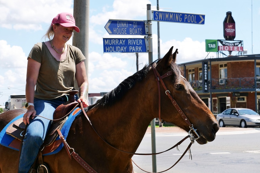 A horse with a female rider stands across the road from a pub.