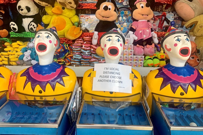 Three open-mouthed fake clowns at the show. One has a paper sign taped to it reading "I'm social distancing".