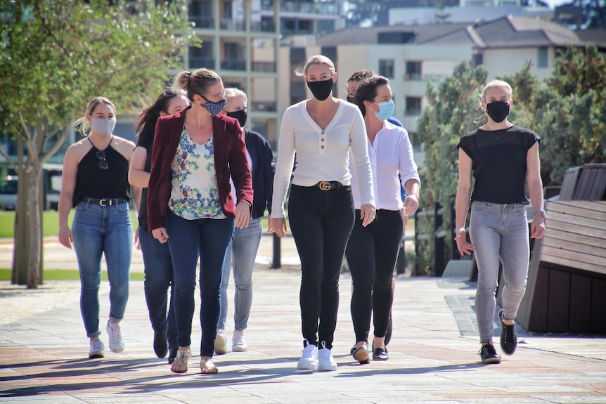 A group of women, all wearing face masks, walk along a path outdoors