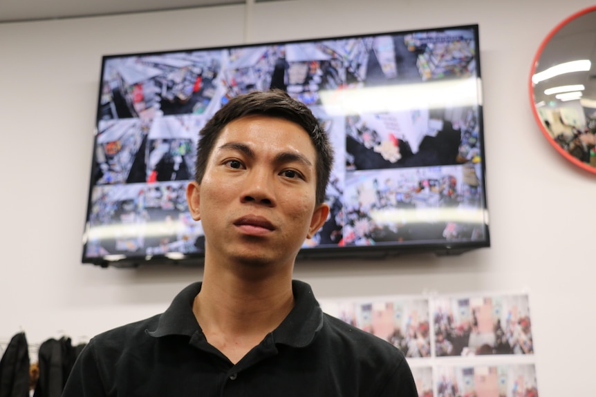 A man of Asian descent standing in front of a screen with multiple CCTV streams on display