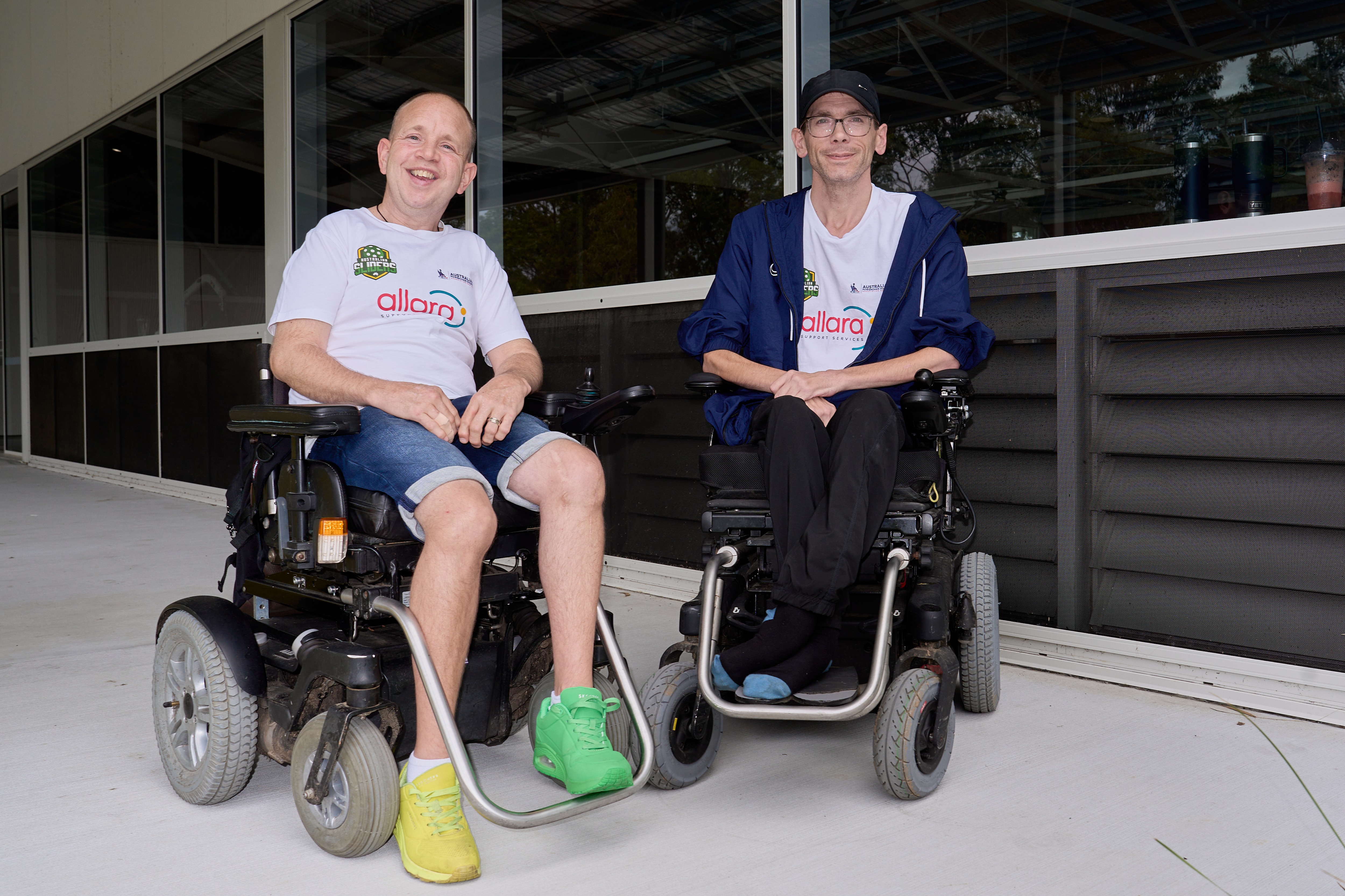 Berrie de blusa branca e shorts em uma cadeira de rodas, Marcel de boné e moletom com capuz em uma cadeira de rodas ao ar livre
