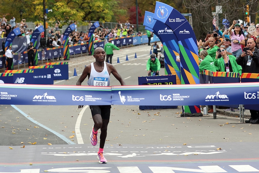 Un corredor de maratón mira hacia abajo cuando está a punto de romper la cinta en la línea de meta de una gran carrera.