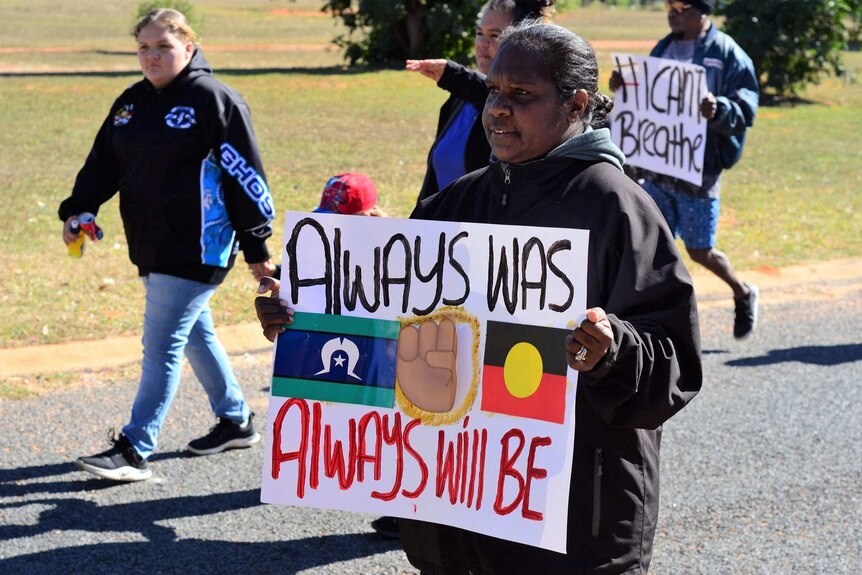 Woorabinda woman with handmade "always was, always will be" sign, walks with other protesters, #ICan'tBreathe sign behind.