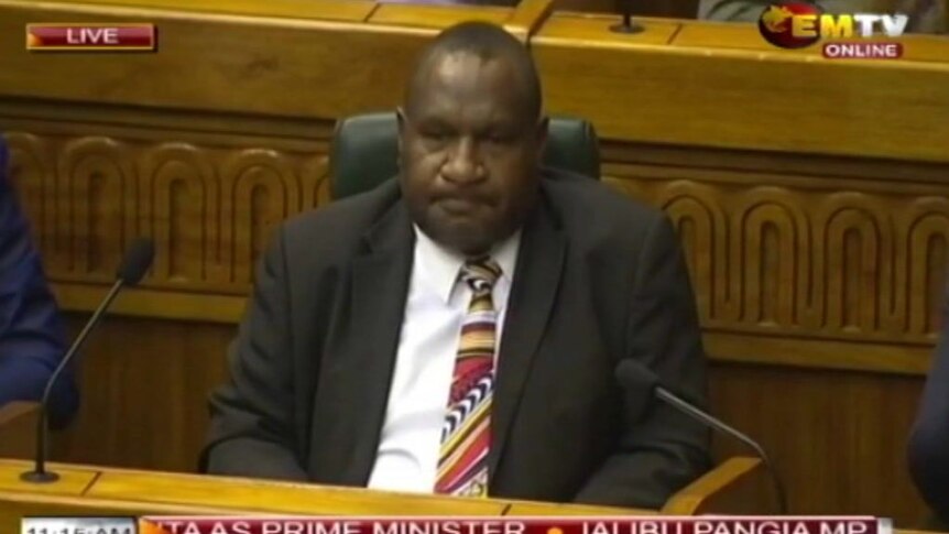 James Marape with lips curled behind microphones.