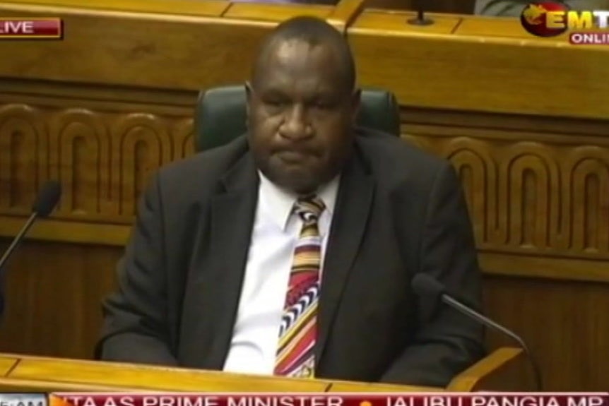 James Marape with lips curled behind microphones.