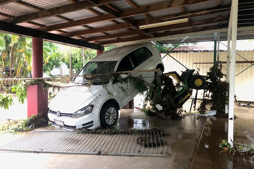 A car leaning on its front nose and back raised against the back of a carport.