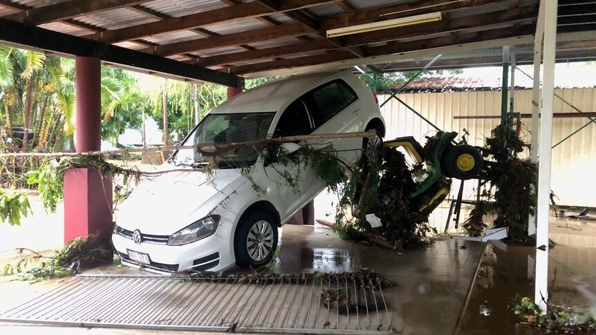 A car leaning on its front nose and back raised against the back of a carport.