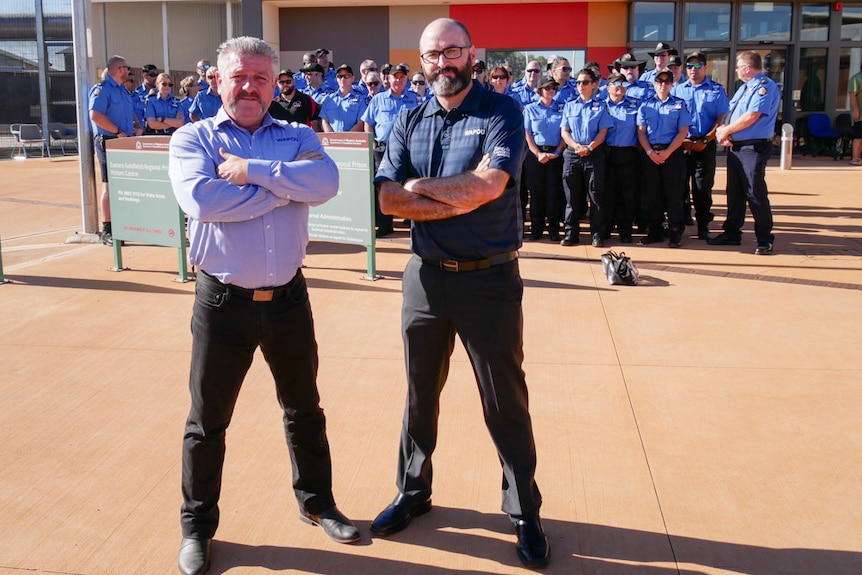 Two men stand in front of a group of striking prison officers