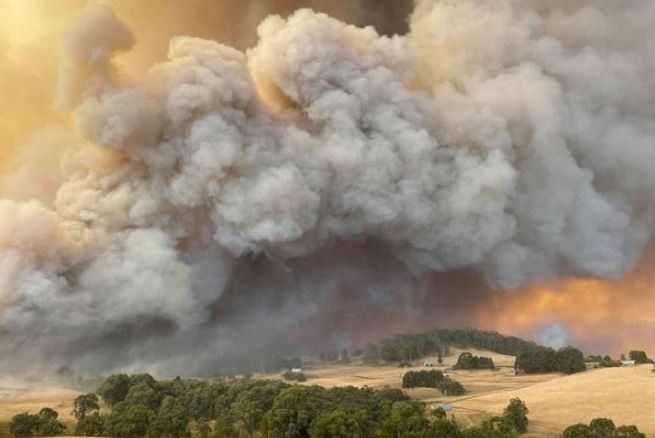 A large plume of smoke and fire can be seen over a rural setting.